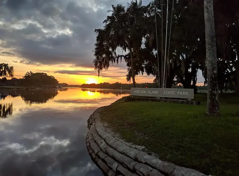 Hontoon Island State Park sign on shore of waterway with sunset in background.