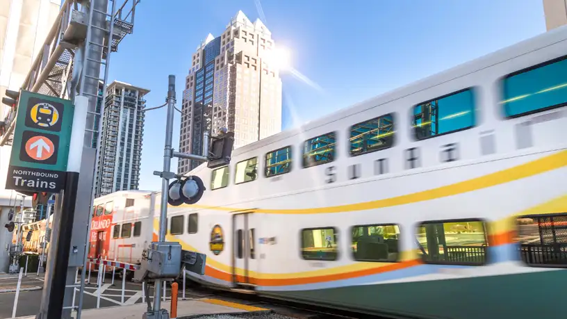 SunRail train travels through Downtown Orlando, with skyscrapers in background.