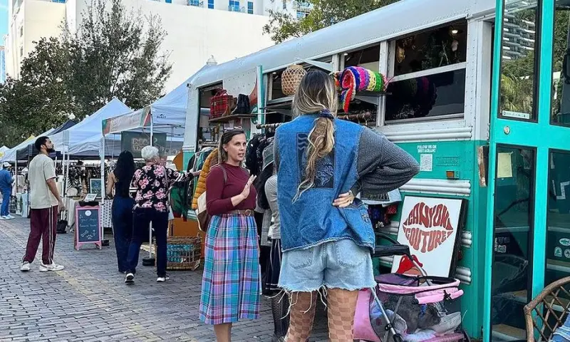 People shopping at outdoor vendor stalls and a vintage bus boutique during the Thornton Park District Night Market.
