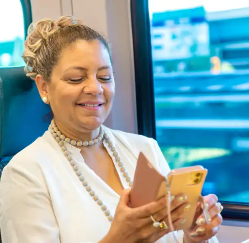 Woman riding SunRail smiling while using her smartphone and wallet during travel.