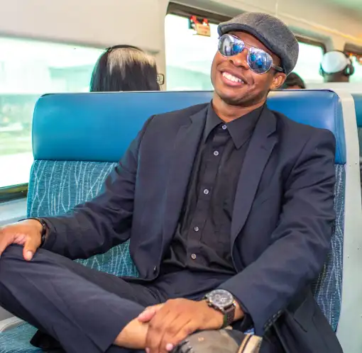 Passenger relaxing in a SunRail seat wearing sunglasses and smiling during the ride.