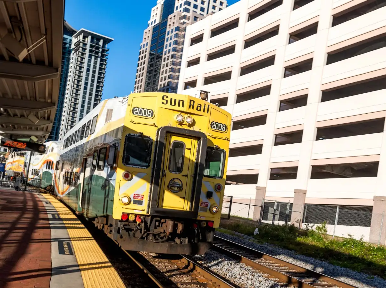 SunRail commuter train departing downtown station platform with city buildings and track in view