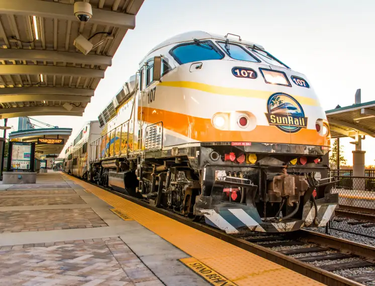 SunRail train arriving at a station platform during daylight with passengers waiting nearby.